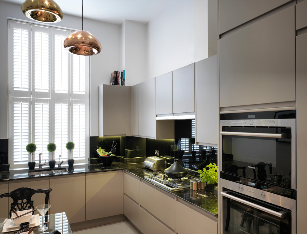 Contemporary kitchen/diner in London with a submerged sink, flat-panel cabinets, beige cabinets, black splashback, glass sheet splashback and stainless steel appliances.