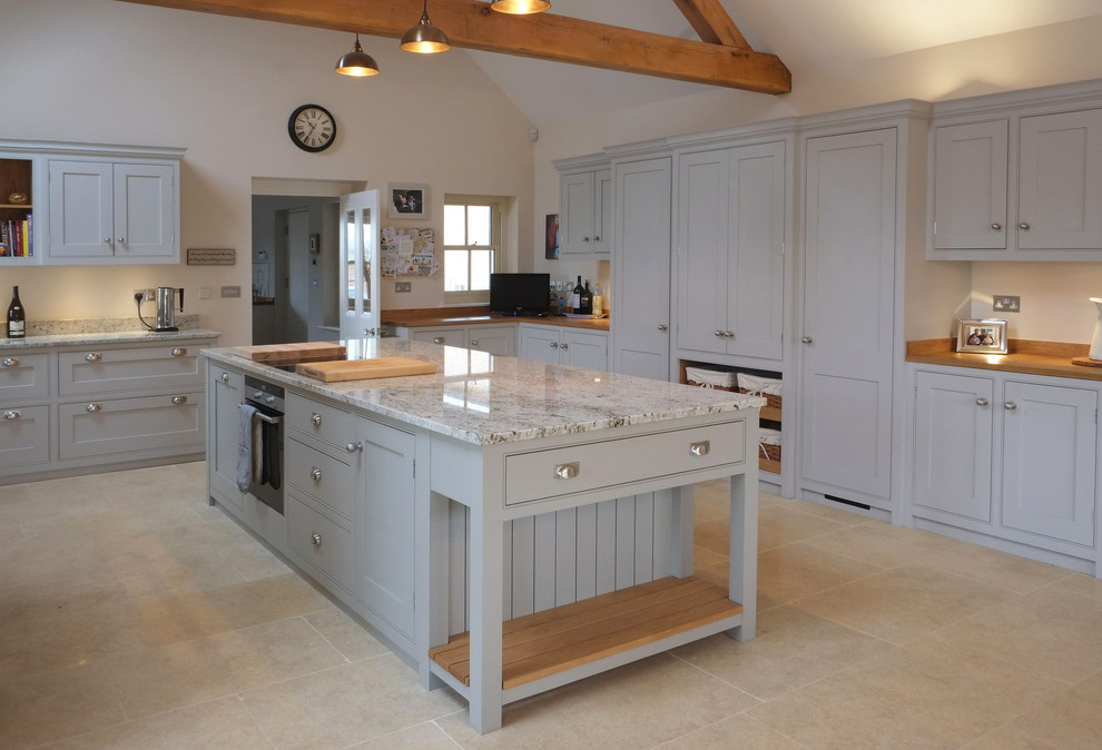 Photo of a large classic u-shaped open plan kitchen in Other with a belfast sink, beaded cabinets, grey cabinets, granite worktops, grey splashback, stone slab splashback, black appliances, limestone flooring and an island.