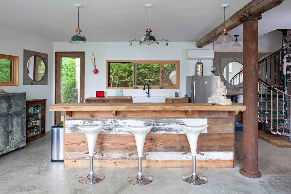 Foto på ett industriellt kök, med en rustik diskho, träbänkskiva, rostfria vitvaror, betonggolv och en köksö