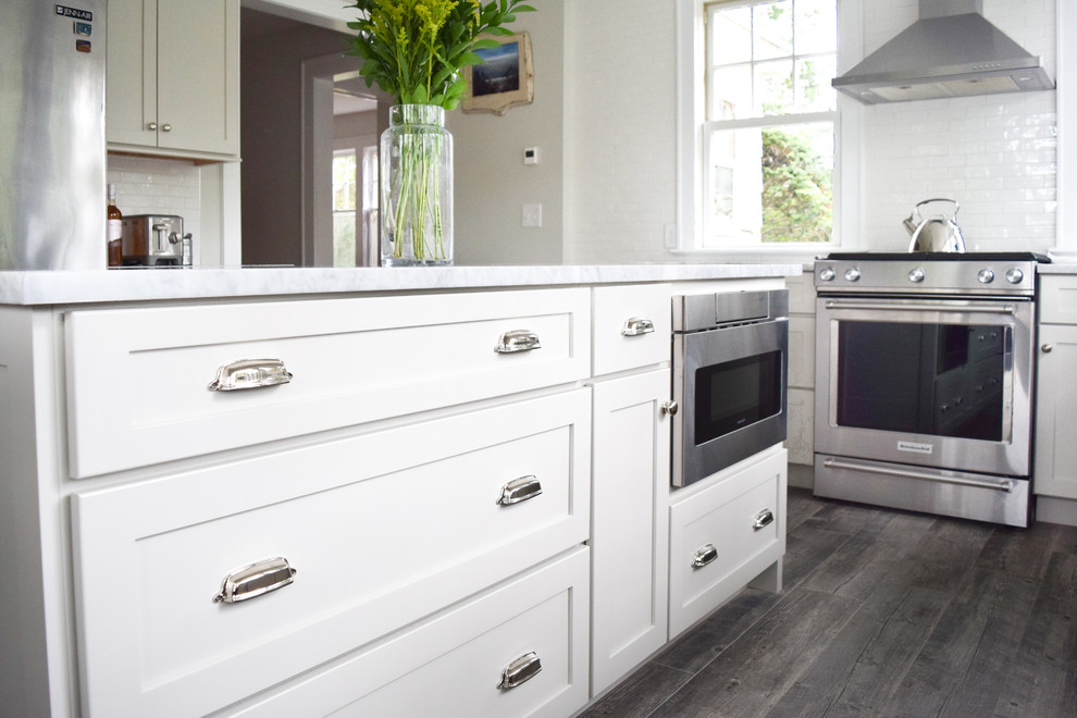 Example of a mid-sized cottage l-shaped porcelain tile and gray floor eat-in kitchen design in New York with a farmhouse sink, shaker cabinets, gray cabinets, marble countertops, white backsplash, subway tile backsplash, stainless steel appliances and an island