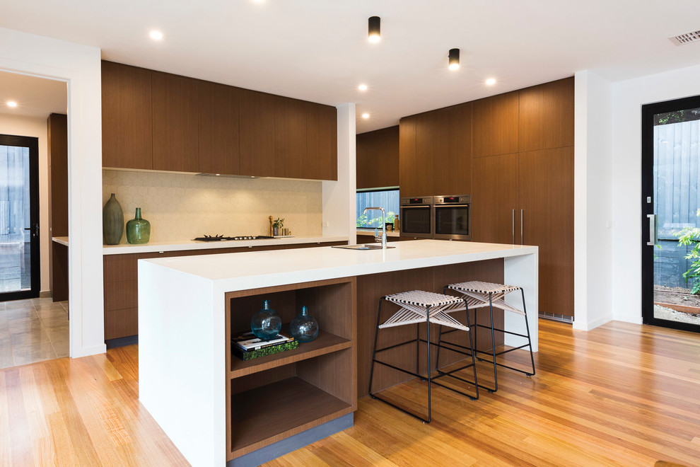 Photo of a contemporary kitchen in Melbourne with a single-bowl sink, flat-panel cabinets, dark wood cabinets, beige splashback, medium hardwood flooring, an island, white worktops and integrated appliances.