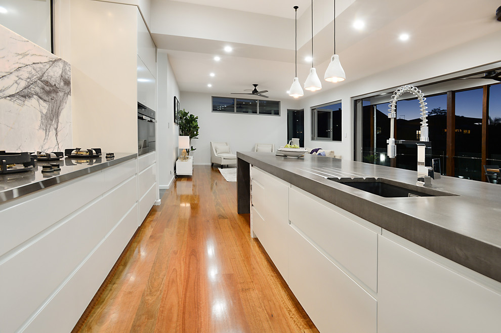 Immagine di un cucina con isola centrale design con top in cemento, ante lisce, ante bianche, paraspruzzi bianco, pavimento in legno massello medio e pavimento marrone