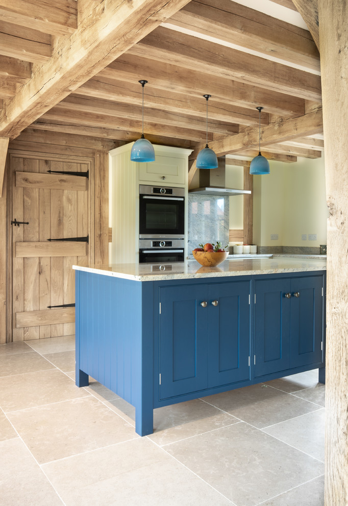 Farmhouse galley kitchen in West Midlands with shaker cabinets, blue cabinets, white splashback, stone slab splashback, stainless steel appliances, an island, beige floors and white worktops.