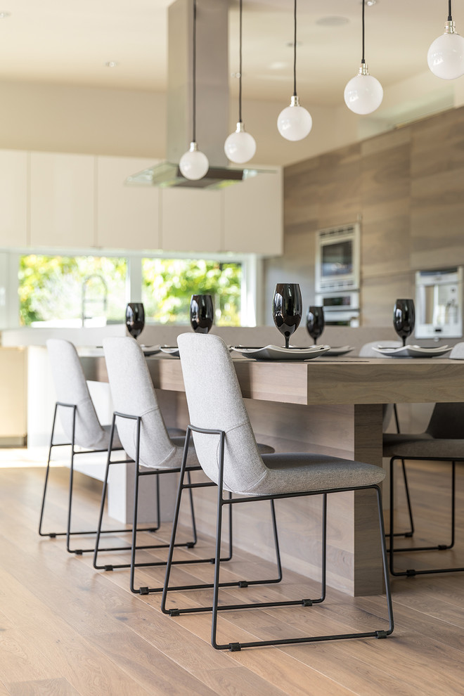 This is an example of an expansive contemporary l-shaped kitchen/diner in Vancouver with a submerged sink, flat-panel cabinets, grey cabinets, quartz worktops, window splashback, stainless steel appliances, medium hardwood flooring, multiple islands and brown floors.