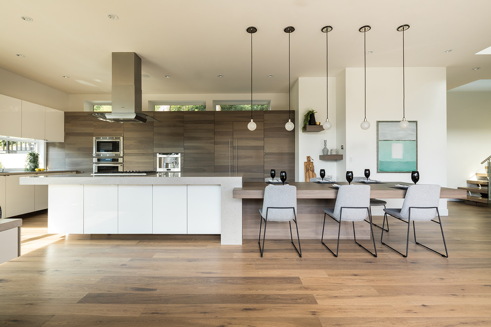 Photo of an expansive contemporary l-shaped kitchen/diner in Vancouver with a submerged sink, flat-panel cabinets, grey cabinets, quartz worktops, window splashback, stainless steel appliances, medium hardwood flooring, multiple islands and brown floors.
