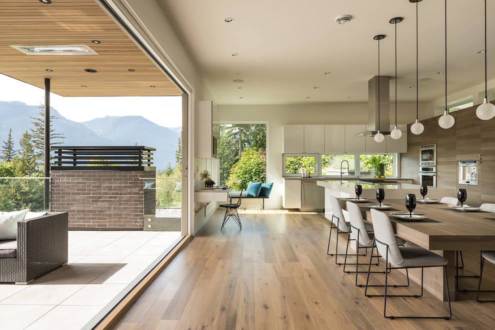 Photo of an expansive contemporary l-shaped kitchen/diner in Vancouver with medium hardwood flooring, brown floors, a submerged sink, flat-panel cabinets, grey cabinets, quartz worktops, window splashback, stainless steel appliances and multiple islands.