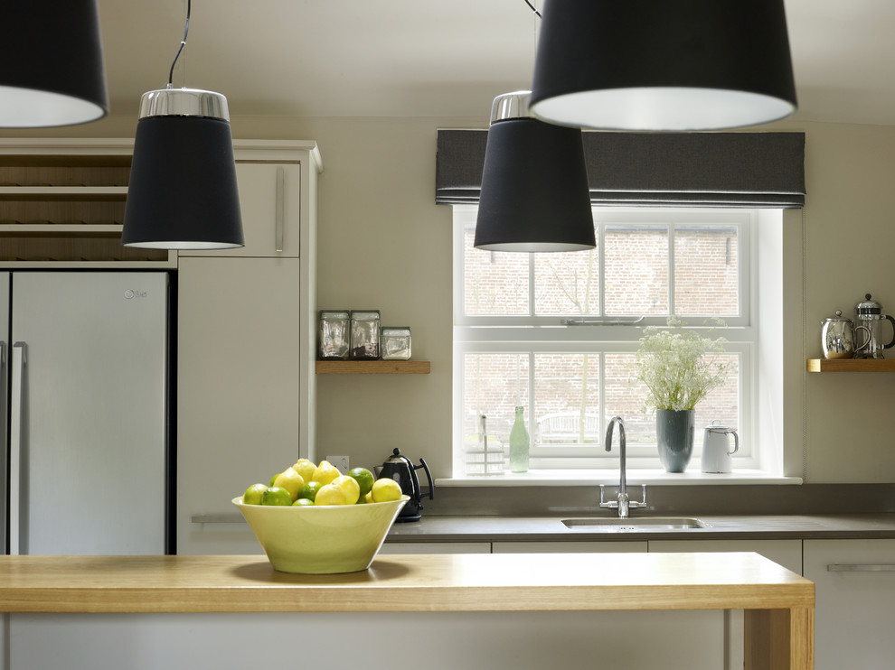 This is an example of a medium sized rural kitchen/diner in London with a submerged sink, flat-panel cabinets, grey cabinets, engineered stone countertops, grey splashback, glass sheet splashback, stainless steel appliances and an island.