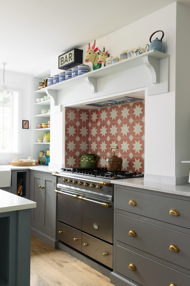 Example of a mid-sized farmhouse l-shaped medium tone wood floor eat-in kitchen design in Other with a double-bowl sink, shaker cabinets, gray cabinets, orange backsplash, ceramic backsplash, stainless steel appliances and an island