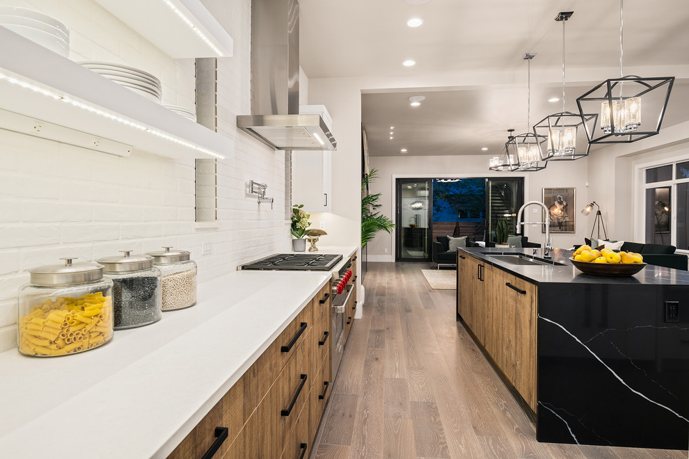 This is an example of a medium sized contemporary open plan kitchen in Seattle with flat-panel cabinets, light wood cabinets, white splashback, brick splashback, stainless steel appliances, medium hardwood flooring and an island.
