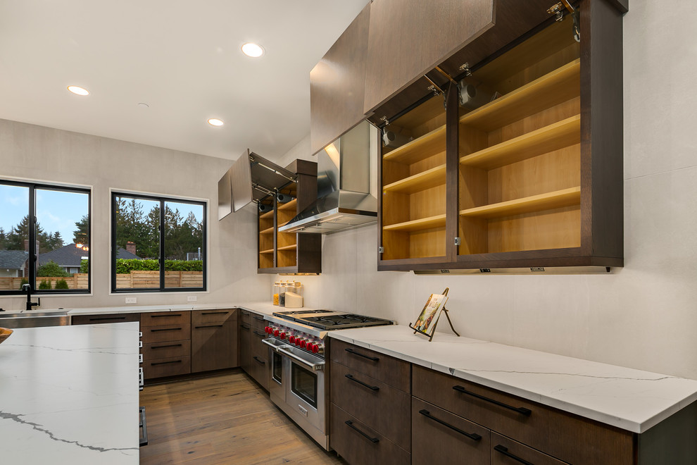 This is an example of a large contemporary l-shaped kitchen/diner in Seattle with a belfast sink, flat-panel cabinets, grey cabinets, engineered stone countertops, grey splashback, stainless steel appliances, medium hardwood flooring, an island, grey floors and white worktops.