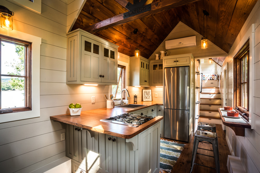 Cette photo montre une cuisine craftsman avec un évier de ferme, un placard à porte shaker, des portes de placard grises, un plan de travail en bois, un électroménager en acier inoxydable, un sol en bois brun et une crédence en lambris de bois.
