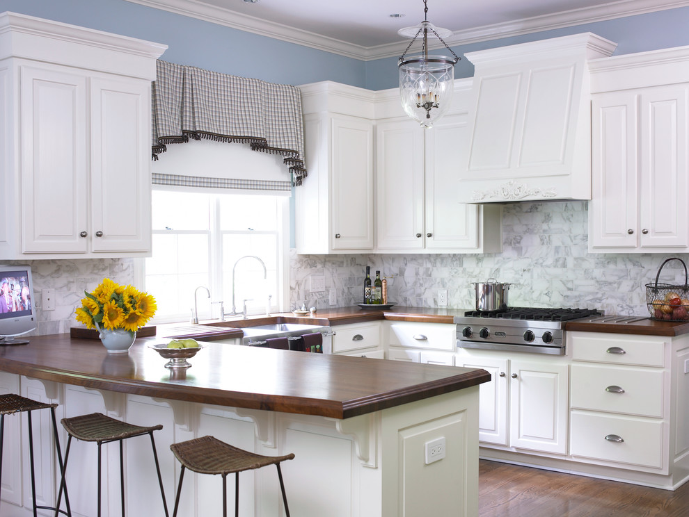 Photo of a traditional u-shaped kitchen in Atlanta with a belfast sink, wood worktops, raised-panel cabinets, white cabinets, white splashback and stone tiled splashback.