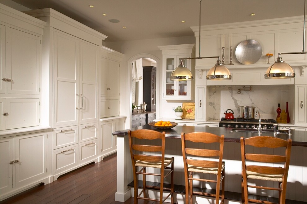 This is an example of a traditional kitchen in Chicago with a submerged sink, shaker cabinets, white cabinets, marble worktops, white splashback, integrated appliances, dark hardwood flooring and an island.