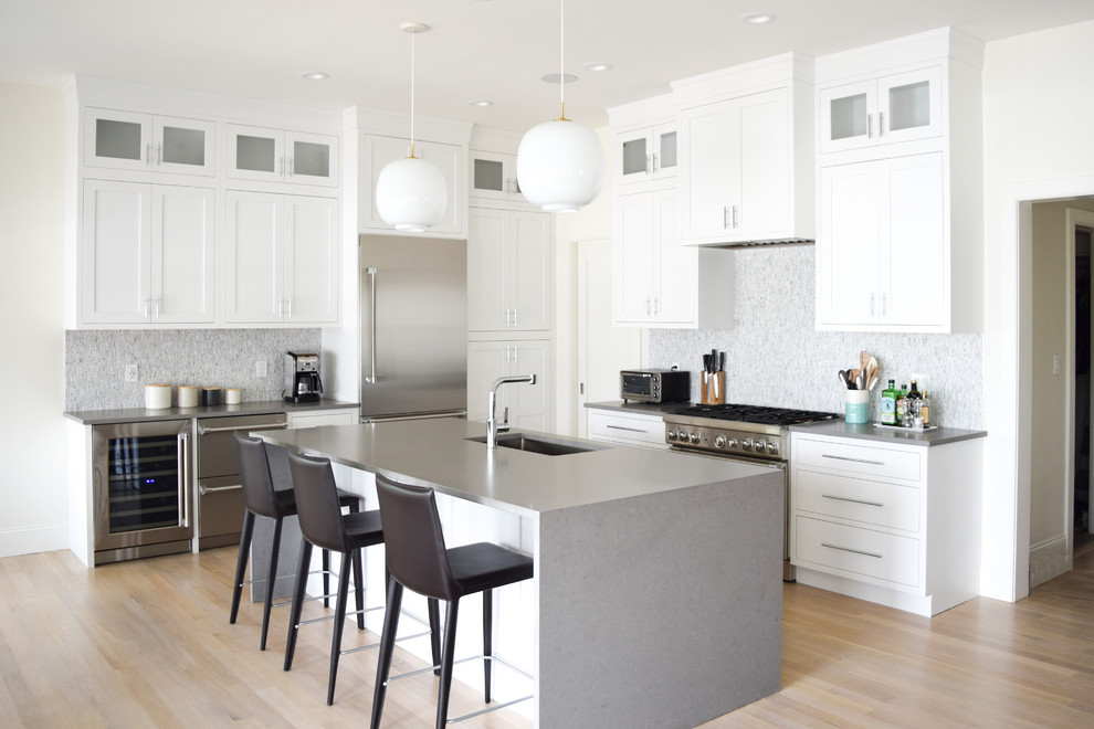 Eat-in kitchen - mid-sized coastal l-shaped light wood floor eat-in kitchen idea in New York with an undermount sink, recessed-panel cabinets, white cabinets, quartz countertops, gray backsplash, marble backsplash, stainless steel appliances and an island