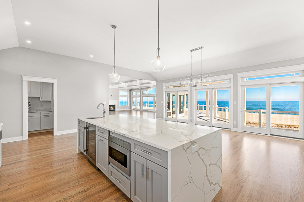 Large beach style l-shaped light wood floor and beige floor kitchen photo in Other with an undermount sink, shaker cabinets, white cabinets, quartz countertops, white backsplash, glass tile backsplash, stainless steel appliances, an island and white countertops