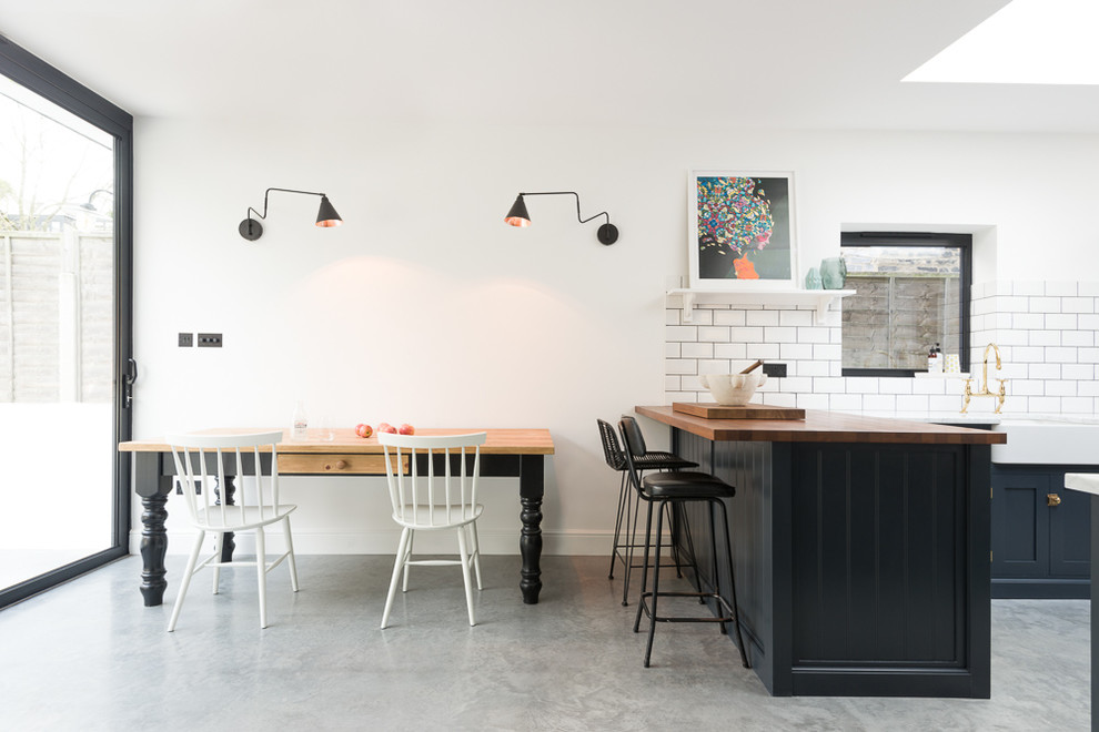 Klassische Küche mit Landhausspüle, Küchenrückwand in Weiß, Rückwand aus Metrofliesen, Schrankfronten mit vertiefter Füllung, blauen Schränken, Arbeitsplatte aus Holz und Halbinsel in London