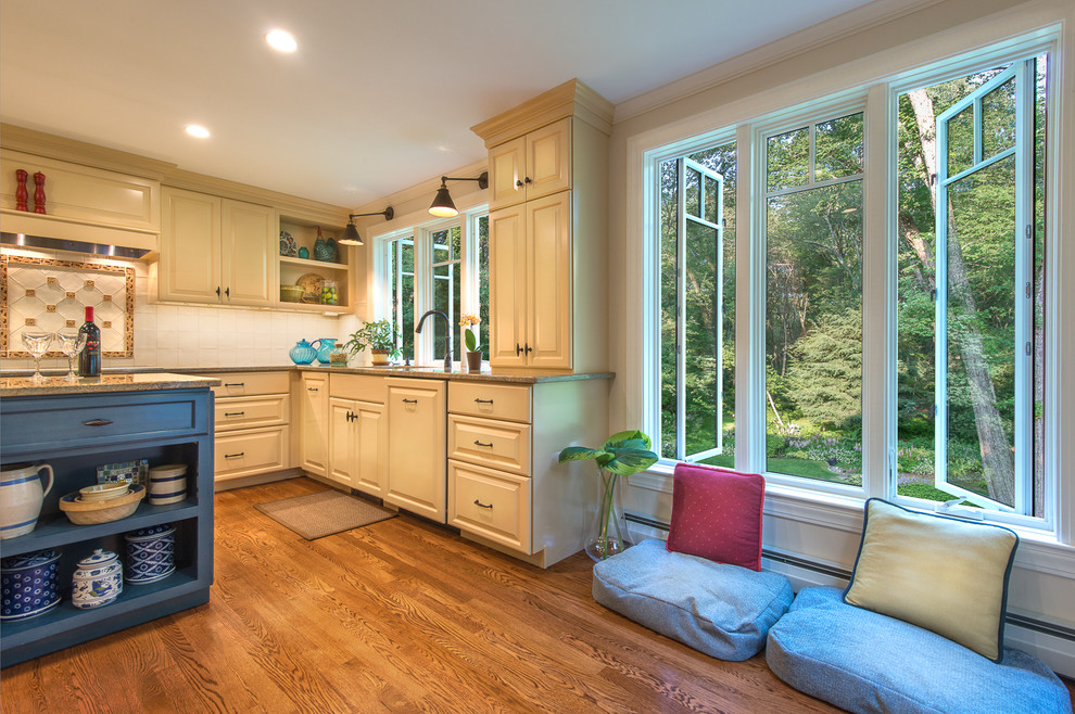 Example of a large eclectic u-shaped medium tone wood floor enclosed kitchen design in Boston with an undermount sink, raised-panel cabinets, yellow cabinets, granite countertops, white backsplash, ceramic backsplash, stainless steel appliances and an island