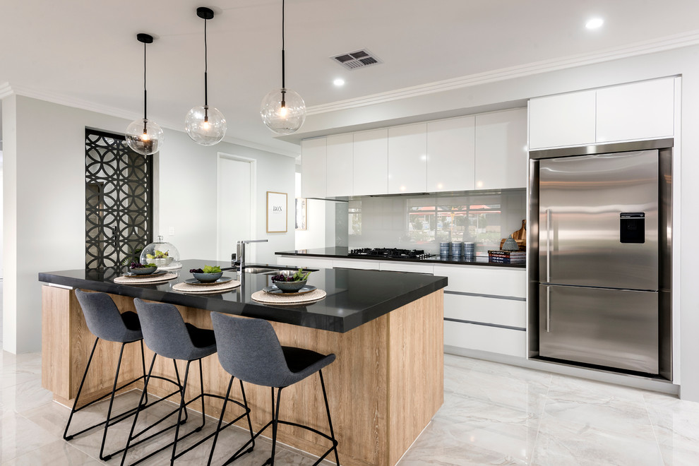 Photo of a large contemporary galley open plan kitchen in Perth with a submerged sink, flat-panel cabinets, light wood cabinets, engineered stone countertops, white splashback, glass sheet splashback, stainless steel appliances, porcelain flooring, an island and white floors.