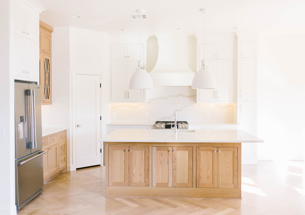 Bild på ett stort lantligt vit vitt kök, med en rustik diskho, skåp i shakerstil, skåp i ljust trä, bänkskiva i kvarts, vitt stänkskydd, stänkskydd i sten, rostfria vitvaror, ljust trägolv, en köksö och brunt golv