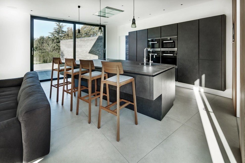 Design ideas for a contemporary open plan kitchen in Hampshire with a built-in sink, flat-panel cabinets, grey cabinets, black appliances, an island, grey floors and grey worktops.