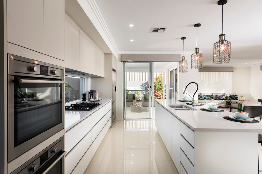 Open concept kitchen - large modern galley porcelain tile and beige floor open concept kitchen idea in Perth with a double-bowl sink, flat-panel cabinets, beige cabinets, quartz countertops, glass sheet backsplash, stainless steel appliances and an island