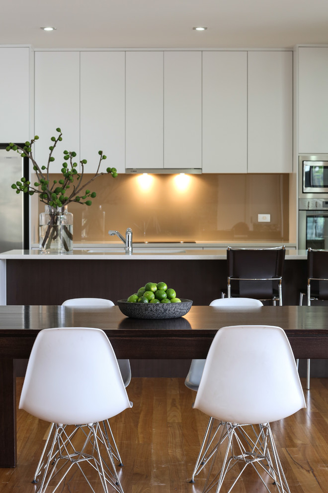 This is an example of a large contemporary galley open plan kitchen in Adelaide with a double-bowl sink, white cabinets, engineered stone countertops, beige splashback, glass sheet splashback, stainless steel appliances, medium hardwood flooring and an island.