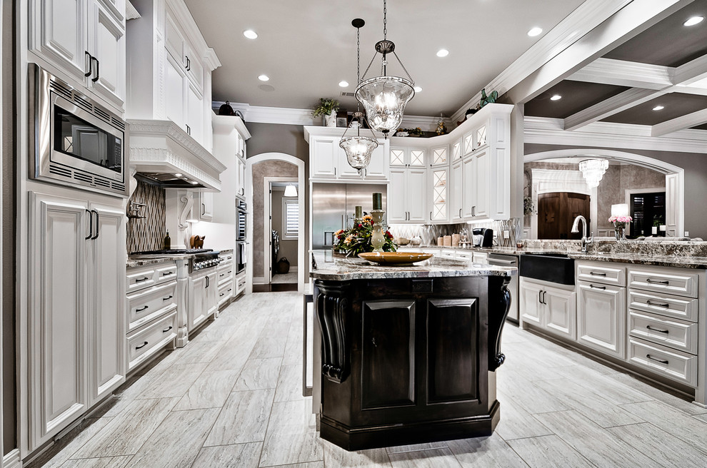 Inredning av ett klassiskt stort flerfärgad flerfärgat kök, med en integrerad diskho, luckor med upphöjd panel, vita skåp, granitbänkskiva, flerfärgad stänkskydd, stänkskydd i glaskakel, rostfria vitvaror, klinkergolv i porslin, en köksö och beiget golv