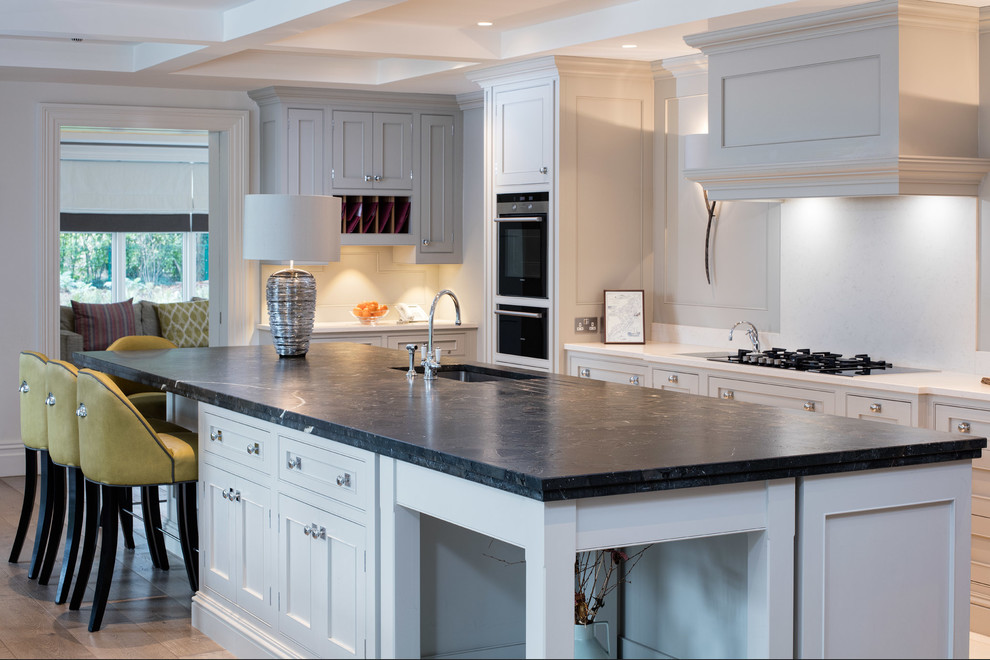 Inspiration for a large timeless u-shaped medium tone wood floor eat-in kitchen remodel in Dublin with an undermount sink, shaker cabinets, limestone countertops, stone slab backsplash, black appliances and an island
