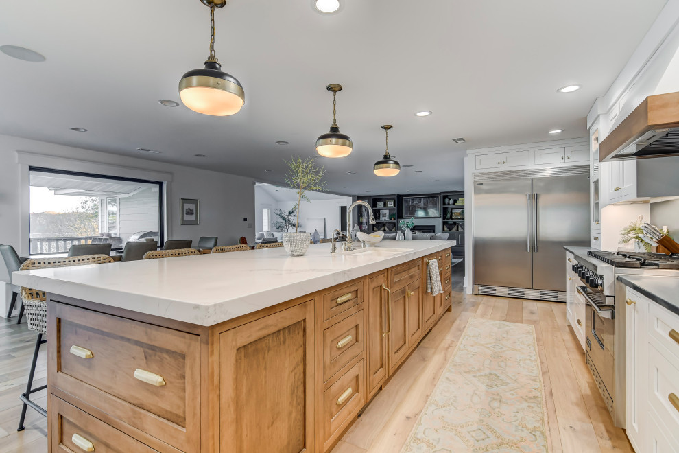 Bild på ett stort amerikanskt vit vitt kök, med en undermonterad diskho, luckor med profilerade fronter, vita skåp, bänkskiva i kvarts, blått stänkskydd, stänkskydd i sten, rostfria vitvaror, ljust trägolv, en köksö och brunt golv