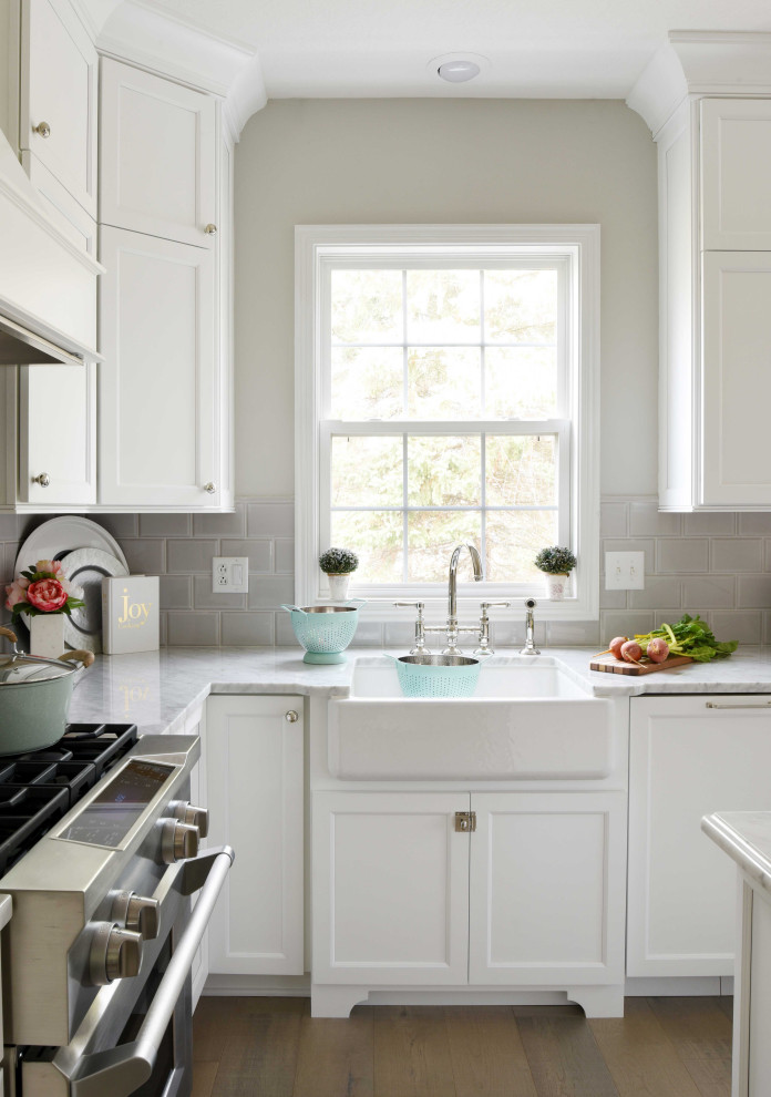 Bild på ett stort lantligt vit vitt kök, med en rustik diskho, skåp i shakerstil, vita skåp, marmorbänkskiva, grått stänkskydd, stänkskydd i tunnelbanekakel, rostfria vitvaror, mellanmörkt trägolv, en köksö och brunt golv