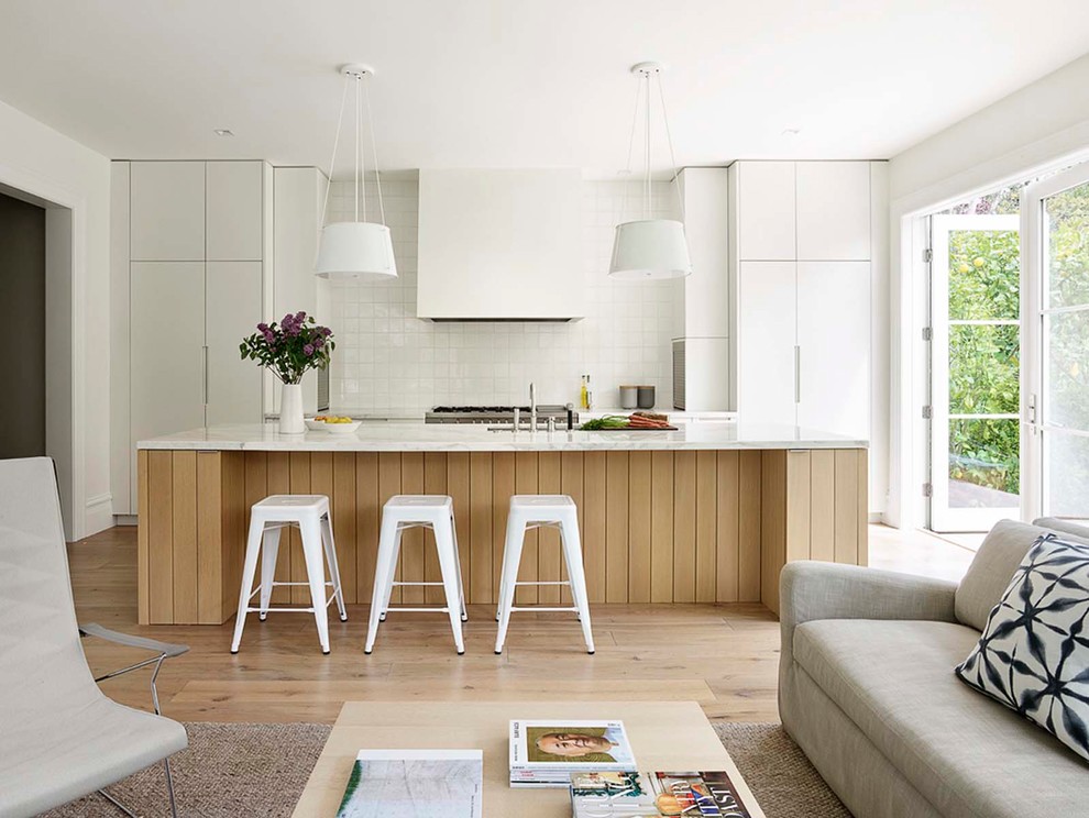 Inspiration för minimalistiska vitt kök med öppen planlösning, med en undermonterad diskho, släta luckor, vita skåp, vitt stänkskydd, rostfria vitvaror, ljust trägolv, en köksö och beiget golv