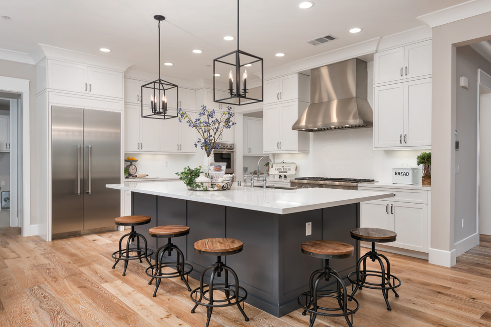 Example of a transitional light wood floor kitchen design in San Francisco with shaker cabinets, white cabinets, white backsplash, stainless steel appliances and an island