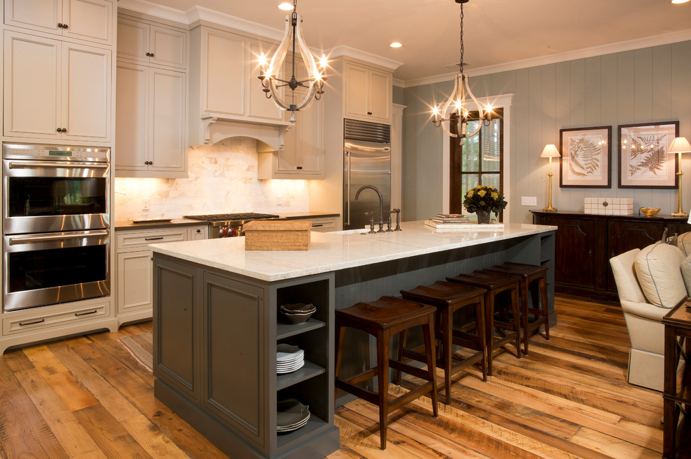 Example of a mid-sized classic l-shaped medium tone wood floor and brown floor open concept kitchen design in Charleston with a farmhouse sink, recessed-panel cabinets, white cabinets, granite countertops, beige backsplash, porcelain backsplash, stainless steel appliances and an island