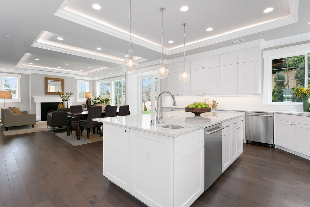 Arts and crafts l-shaped medium tone wood floor and brown floor eat-in kitchen photo in Seattle with a drop-in sink, raised-panel cabinets, white cabinets, quartz countertops, white backsplash, stainless steel appliances and an island