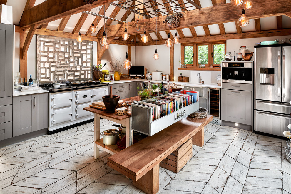 Example of a country l-shaped white floor kitchen design in Hampshire with a farmhouse sink, gray cabinets, an island, shaker cabinets, stainless steel appliances and white countertops