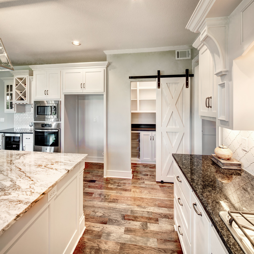 Foto på ett stort vintage kök, med en undermonterad diskho, släta luckor, vita skåp, granitbänkskiva, vitt stänkskydd, stänkskydd i keramik, rostfria vitvaror, mellanmörkt trägolv, en köksö och flerfärgat golv