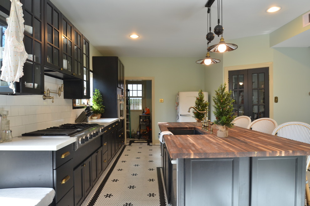 Bild på ett stort eklektiskt linjärt kök med öppen planlösning, med en undermonterad diskho, luckor med glaspanel, svarta skåp, träbänkskiva, vitt stänkskydd, stänkskydd i keramik, rostfria vitvaror, klinkergolv i keramik och en köksö