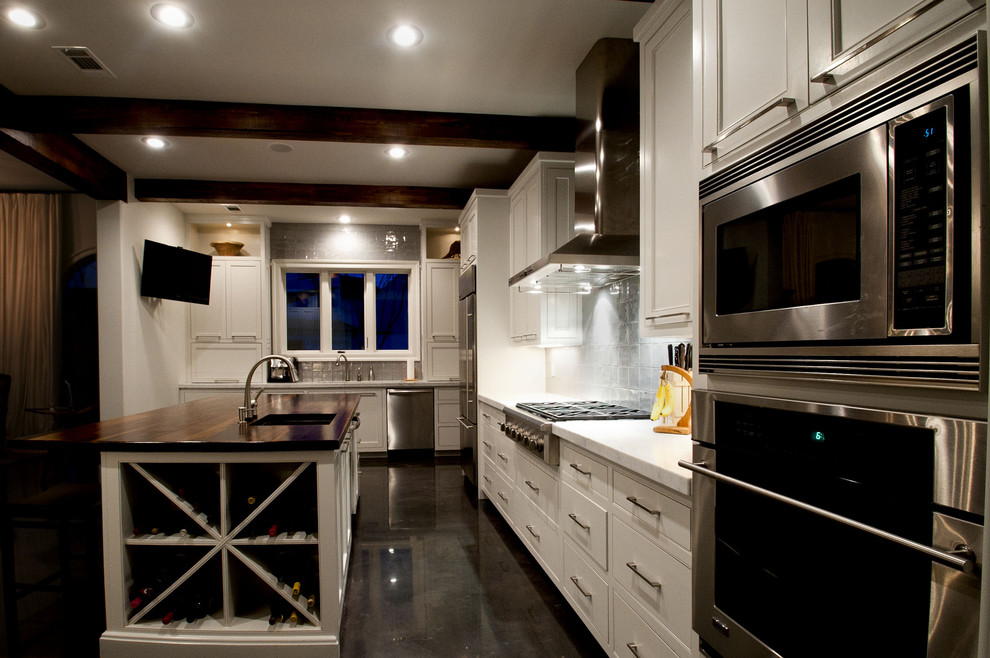 Foto på ett avskilt, stort funkis l-kök, med en undermonterad diskho, skåp i shakerstil, vita skåp, träbänkskiva, grått stänkskydd, stänkskydd i keramik, rostfria vitvaror, betonggolv, en köksö och brunt golv