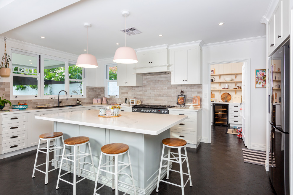 Mid-sized beach style l-shaped dark wood floor and brown floor eat-in kitchen photo in Perth with a double-bowl sink, shaker cabinets, white cabinets, quartz countertops, beige backsplash, mosaic tile backsplash, stainless steel appliances, an island and white countertops