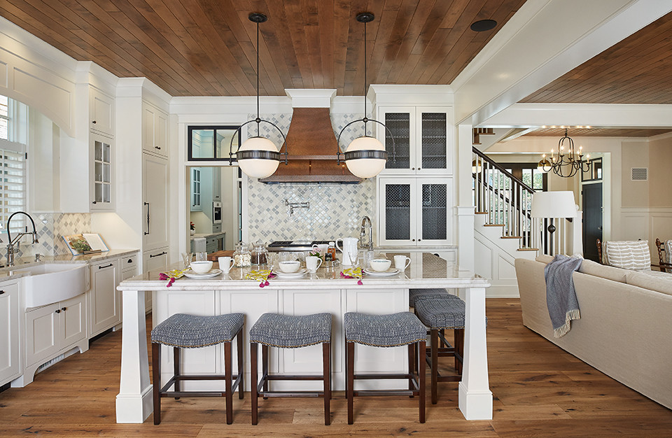 Large transitional l-shaped medium tone wood floor and brown floor open concept kitchen photo in Grand Rapids with a farmhouse sink, recessed-panel cabinets, white cabinets, granite countertops, blue backsplash, ceramic backsplash, paneled appliances, an island and multicolored countertops