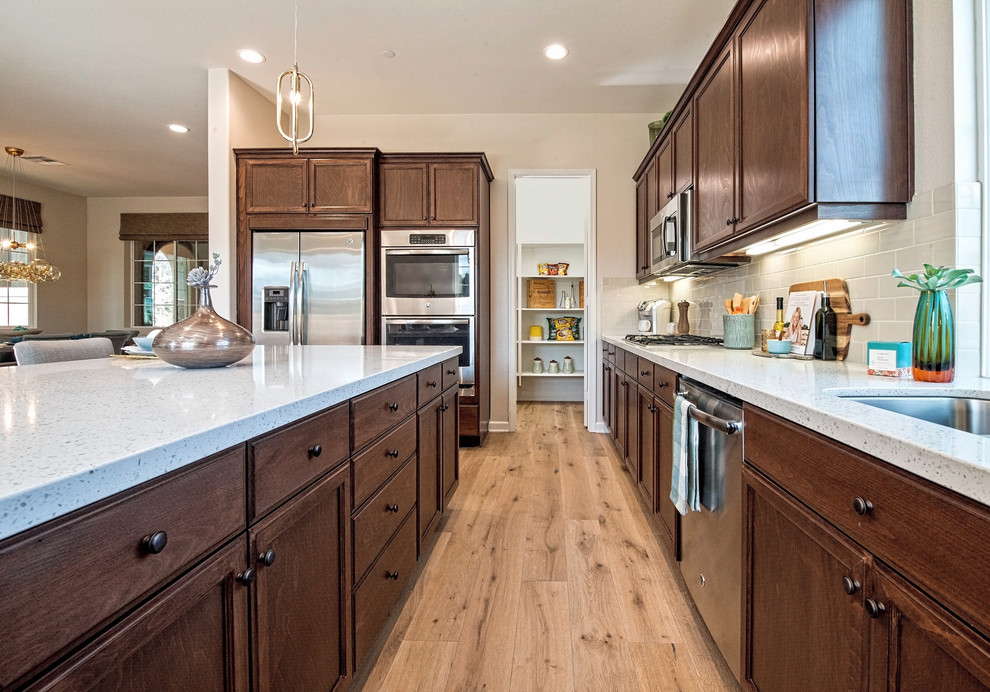 Example of a mid-sized transitional u-shaped light wood floor and beige floor open concept kitchen design in Los Angeles with an undermount sink, recessed-panel cabinets, medium tone wood cabinets, quartz countertops, beige backsplash, subway tile backsplash, stainless steel appliances, an island and white countertops
