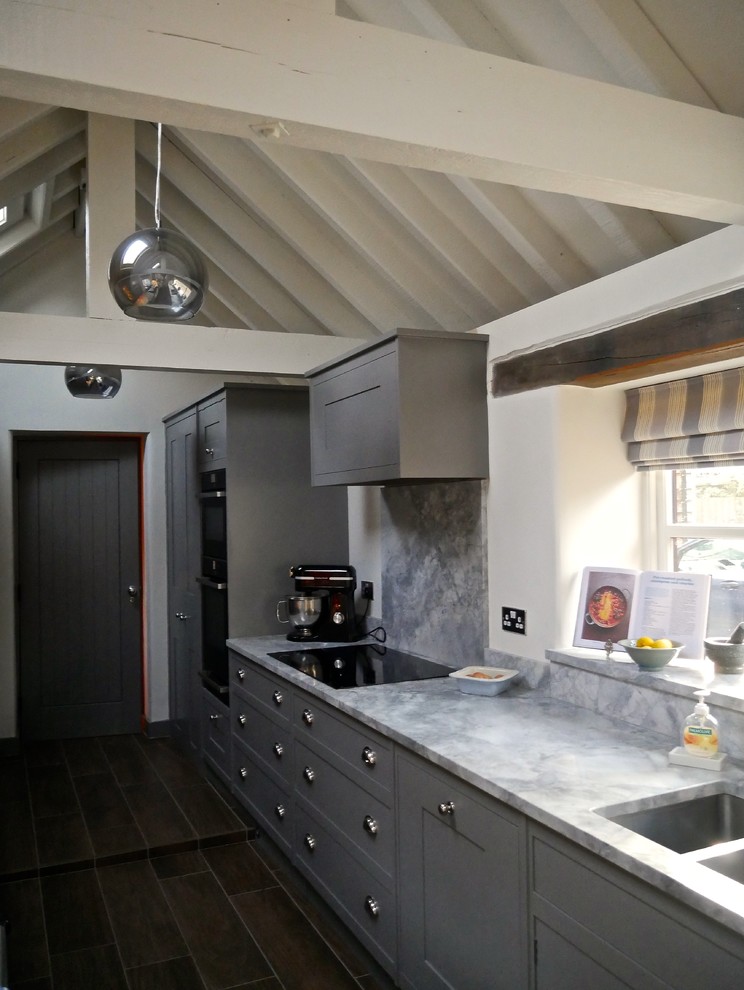 Modern inredning av ett kök, med en nedsänkt diskho, skåp i shakerstil, grå skåp, marmorbänkskiva, grått stänkskydd, svarta vitvaror och klinkergolv i porslin