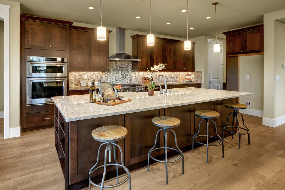 Inspiration for a classic l-shaped open plan kitchen in Seattle with a belfast sink, shaker cabinets, dark wood cabinets, engineered stone countertops, white splashback, mosaic tiled splashback, stainless steel appliances, medium hardwood flooring and an island.