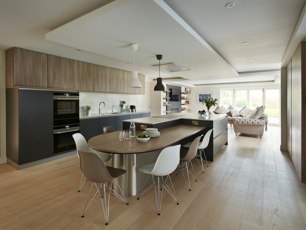 Cette image montre une cuisine ouverte linéaire design en bois clair avec un placard à porte plane, un électroménager noir, parquet clair, îlot et un sol beige.