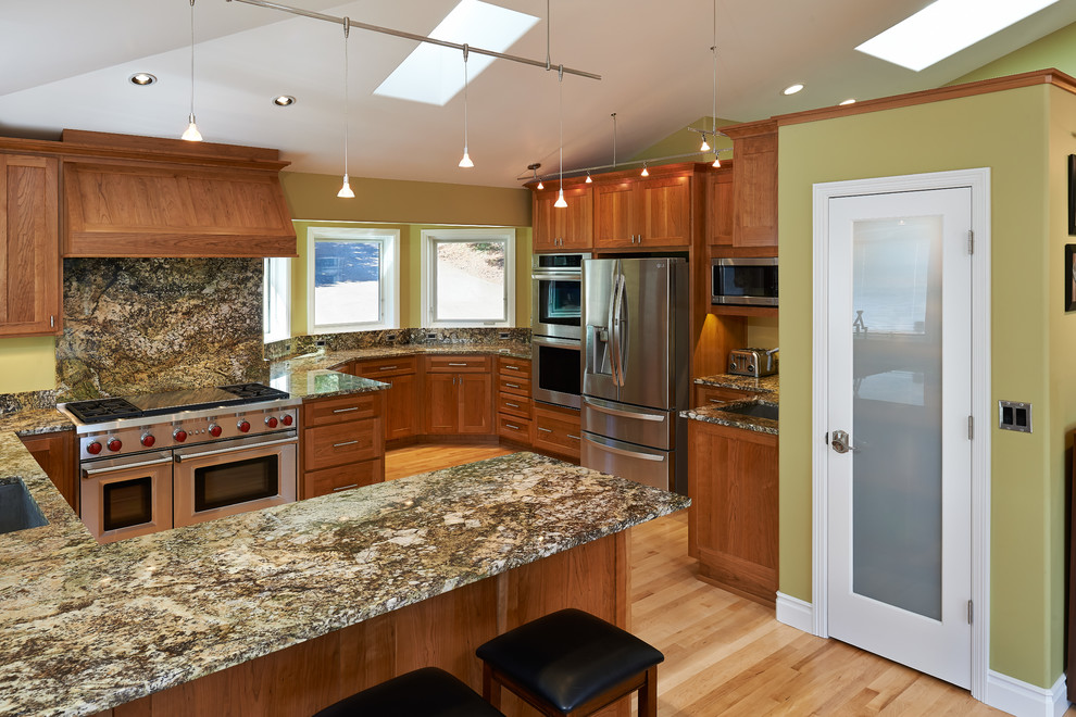 Foto på ett mellanstort amerikanskt kök, med en nedsänkt diskho, luckor med infälld panel, skåp i mellenmörkt trä, granitbänkskiva, stänkskydd med metallisk yta, stänkskydd i sten, rostfria vitvaror, ljust trägolv, en halv köksö och beiget golv