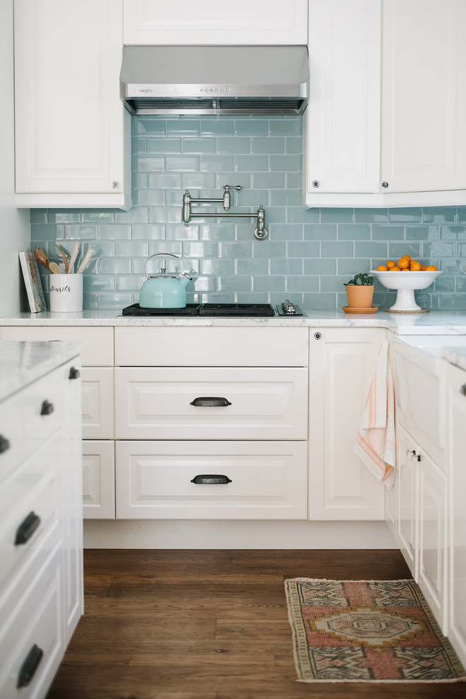 Foto på ett mellanstort lantligt vit kök, med en rustik diskho, luckor med upphöjd panel, vita skåp, marmorbänkskiva, blått stänkskydd, stänkskydd i glaskakel, rostfria vitvaror, mellanmörkt trägolv, en köksö och brunt golv