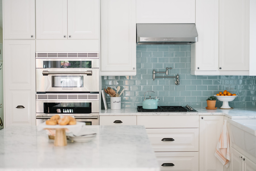 Bild på ett mellanstort lantligt vit vitt kök, med en rustik diskho, luckor med upphöjd panel, vita skåp, marmorbänkskiva, blått stänkskydd, stänkskydd i glaskakel, rostfria vitvaror, mellanmörkt trägolv, en köksö och brunt golv