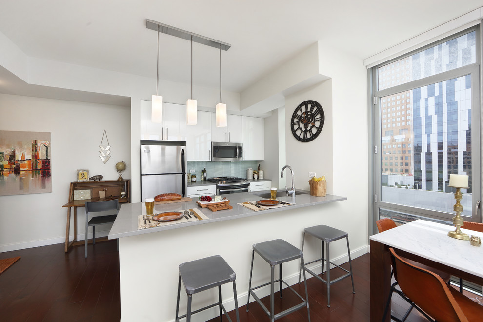 Zweizeilige, Kleine Moderne Küche mit flächenbündigen Schrankfronten, weißen Schränken, Küchengeräten aus Edelstahl, dunklem Holzboden und Halbinsel in New York