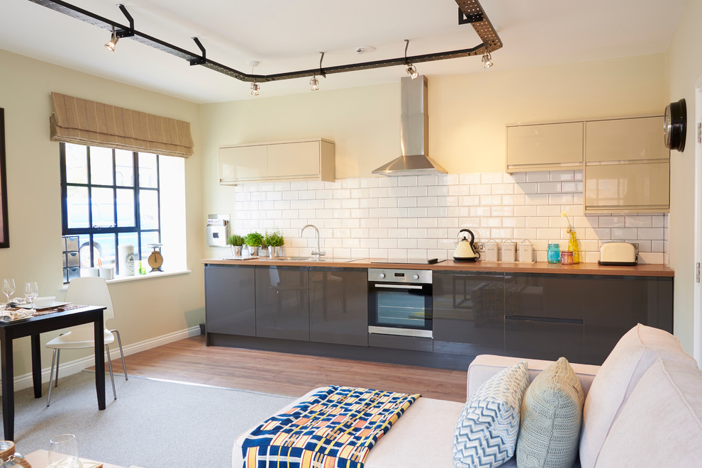 Small industrial grey and cream single-wall open plan kitchen in Other with flat-panel cabinets and white splashback.