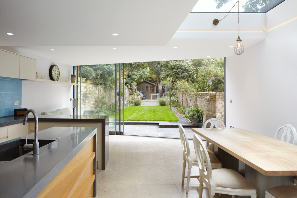 Modern inredning av ett kök och matrum, med en enkel diskho, släta luckor, vita skåp, bänkskiva i betong, blått stänkskydd och en köksö